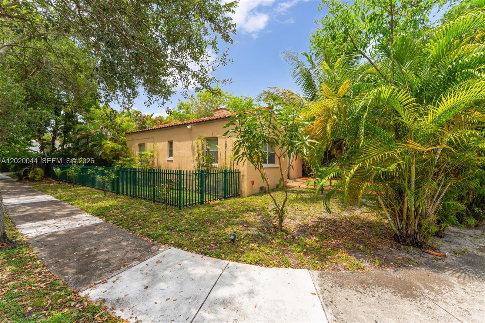 A tan stucco house with a red tile roof sits behind a green metal fence — 28 NE 48th St, Miami FL 33137, MIAMI, FL