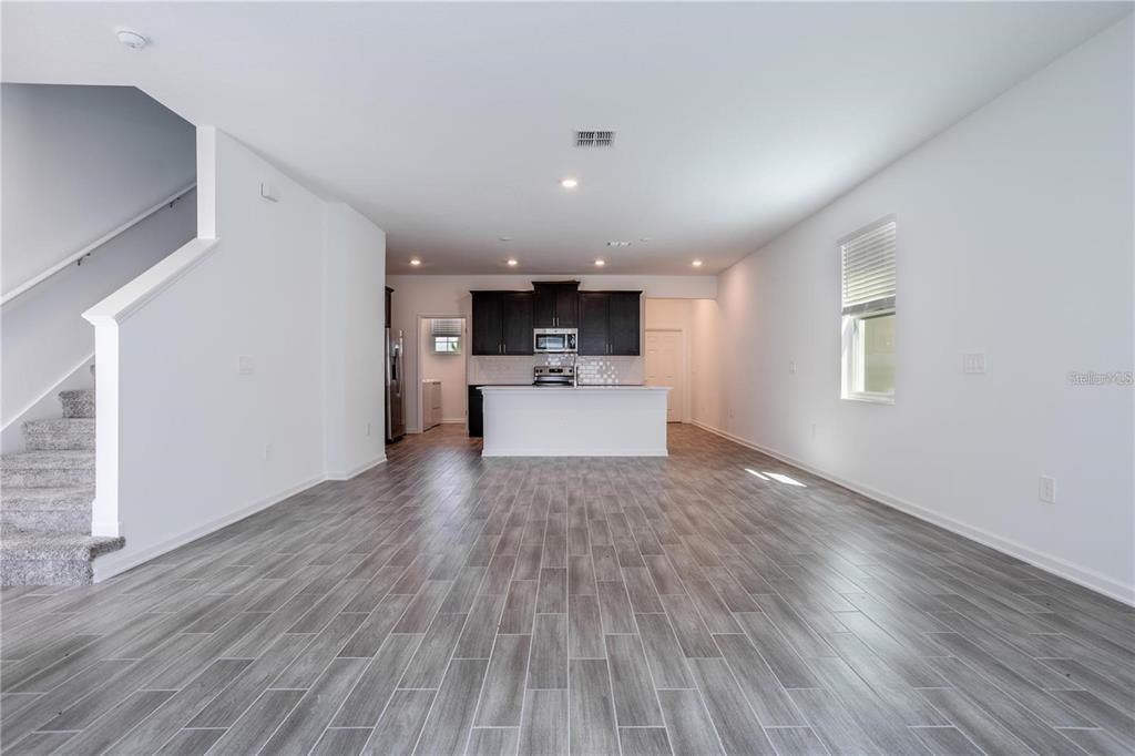 An open-concept living area features gray wood-look tile flooring, white walls, and a kitchen island — 1660 CROSS PRAIRIE PARKWAY, KISSIMMEE, FL