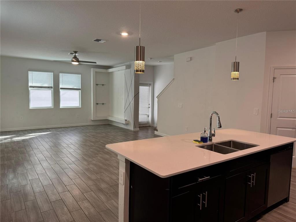 A kitchen island with a sink overlooks an open-concept living area with wood-look tile floors — 1660 CROSS PRAIRIE PARKWAY, KISSIMMEE, FL