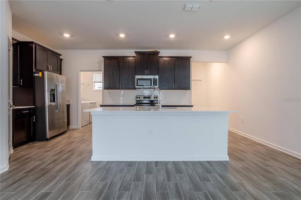 A kitchen features dark wood cabinets, stainless steel appliances, a white island, and gray flooring — 1660 CROSS PRAIRIE PARKWAY, KISSIMMEE, FL