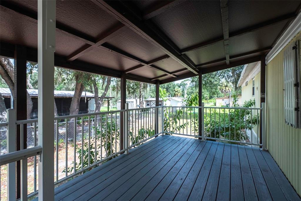 A covered wooden deck with white railings overlooks a backyard with trees and neighboring houses — 6377 W FLANDERS LANE, CRYSTAL RIVER, FL