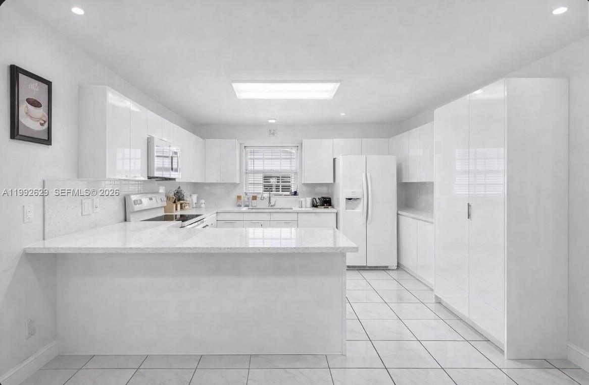 A bright white kitchen features glossy cabinets, quartz countertops, and tiled flooring — 2145 SW 26 ST, Miami FL 33133, MIAMI, FL