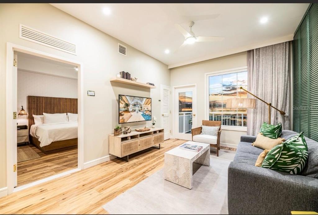 A living room with a sofa, coffee table, TV console, and a view into a bedroom — 3151 SUNSET WALK DRIVE UNIT 402, KISSIMMEE, FL