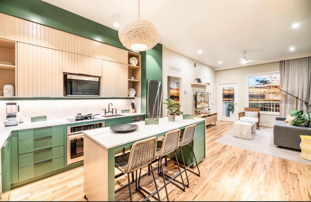 A modern kitchen with green cabinets and a central island opens into a living area — 3151 SUNSET WALK DRIVE UNIT 402, KISSIMMEE, FL