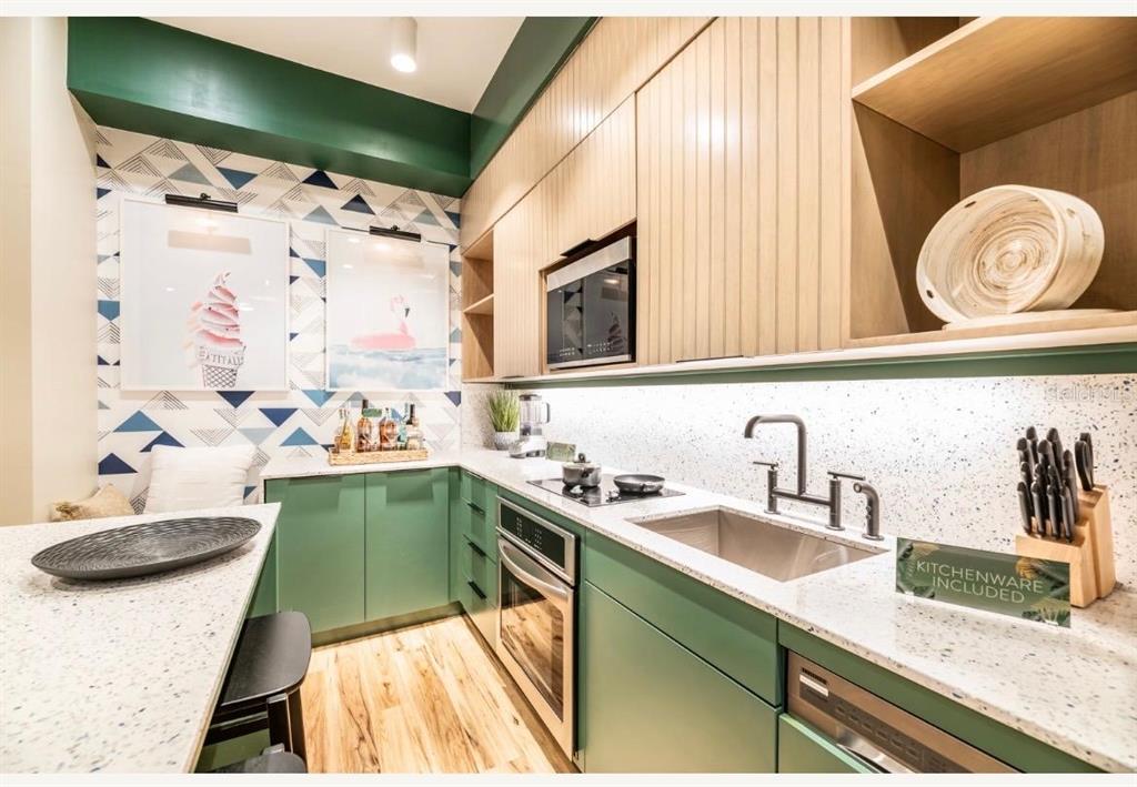 A modern kitchen features green cabinets, light wood upper cabinets, and a patterned accent wall — 3151 SUNSET WALK DRIVE UNIT 402, KISSIMMEE, FL