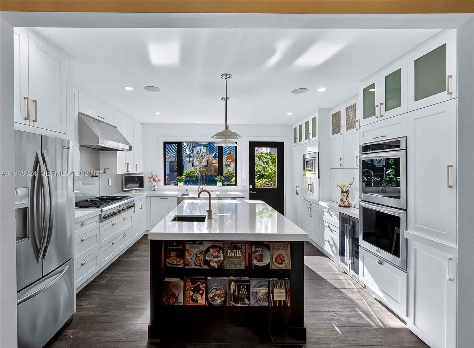 A modern white kitchen features a dark island with built-in shelving and stainless steel appliances — 1680 Onaway Dr, Coconut Grove FL 33133, COCONUT GROVE, FL