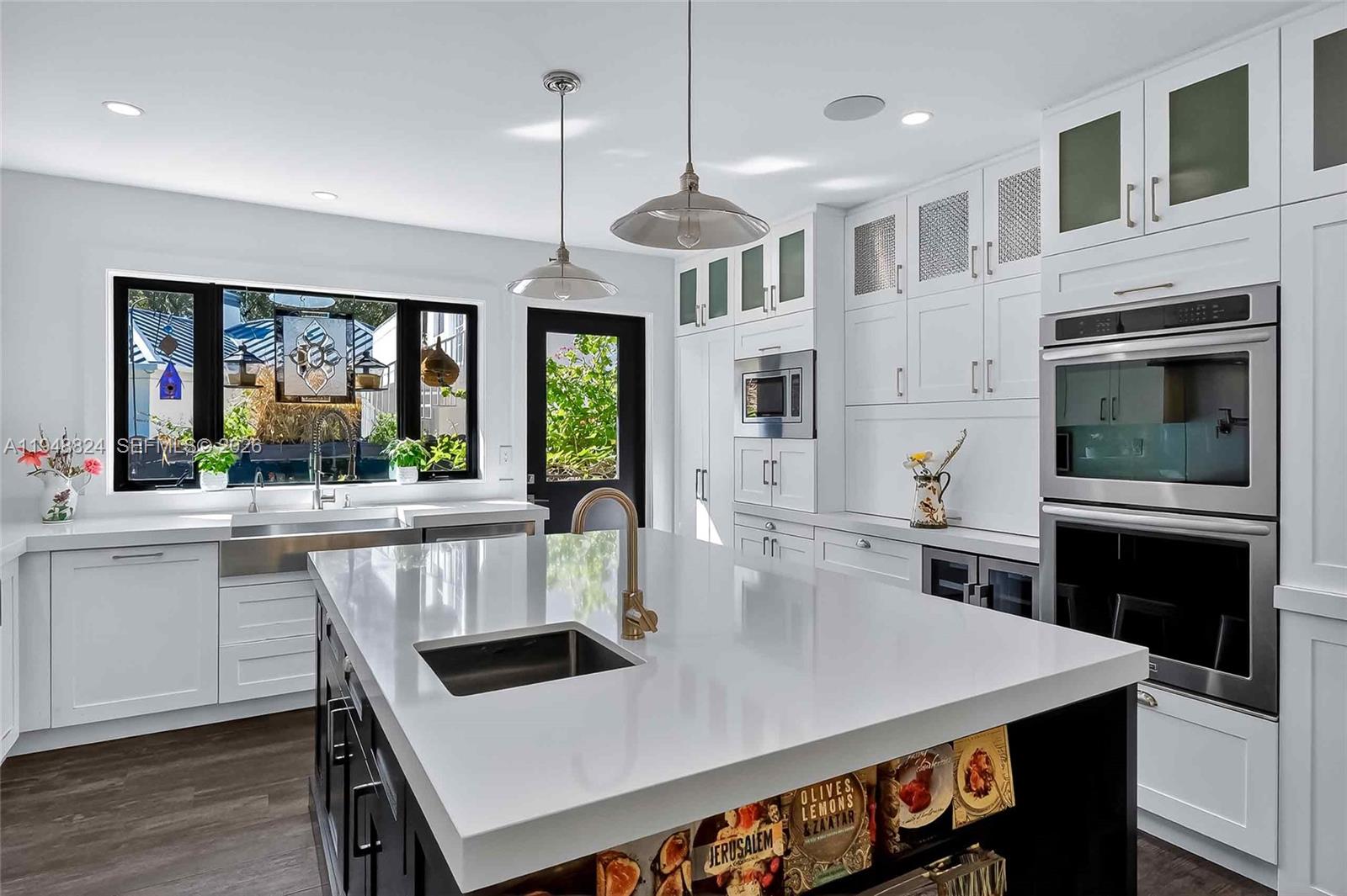 A modern kitchen features white cabinetry, a dark island with a sink, and stainless appliances — 1680 Onaway Dr, Coconut Grove FL 33133, COCONUT GROVE, FL