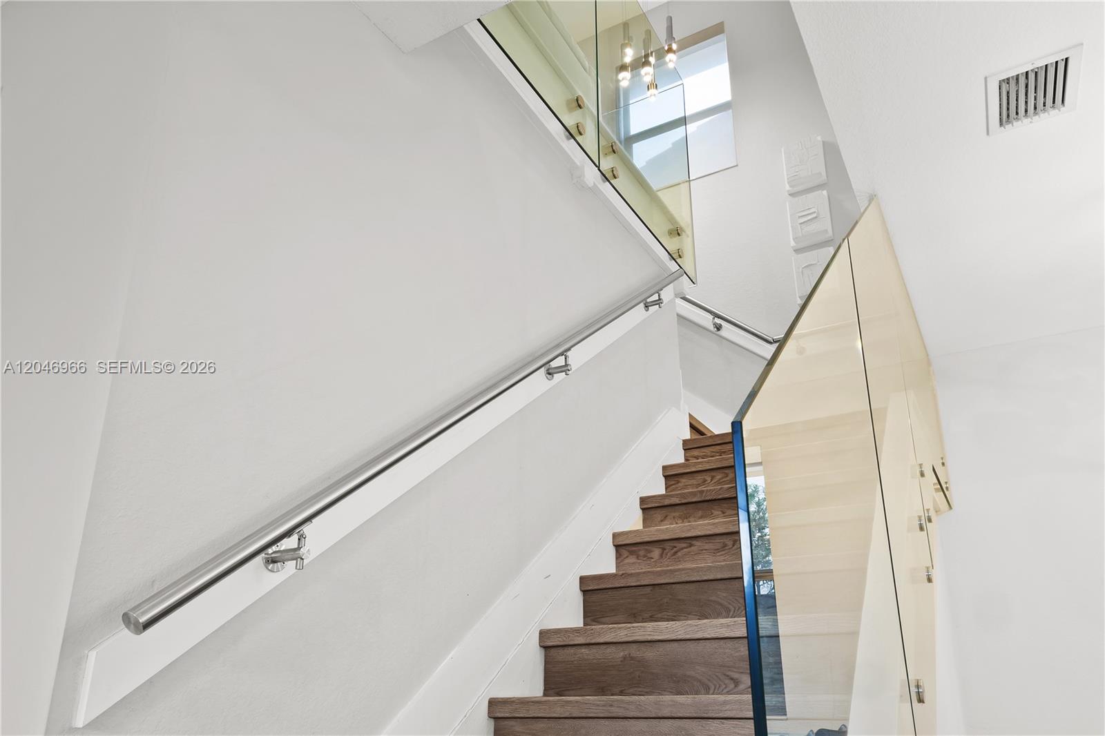 A wooden staircase features a glass railing and a long metal handrail against white walls — 8774 NW 103rd Ave, Doral FL 33178, DORAL, FL