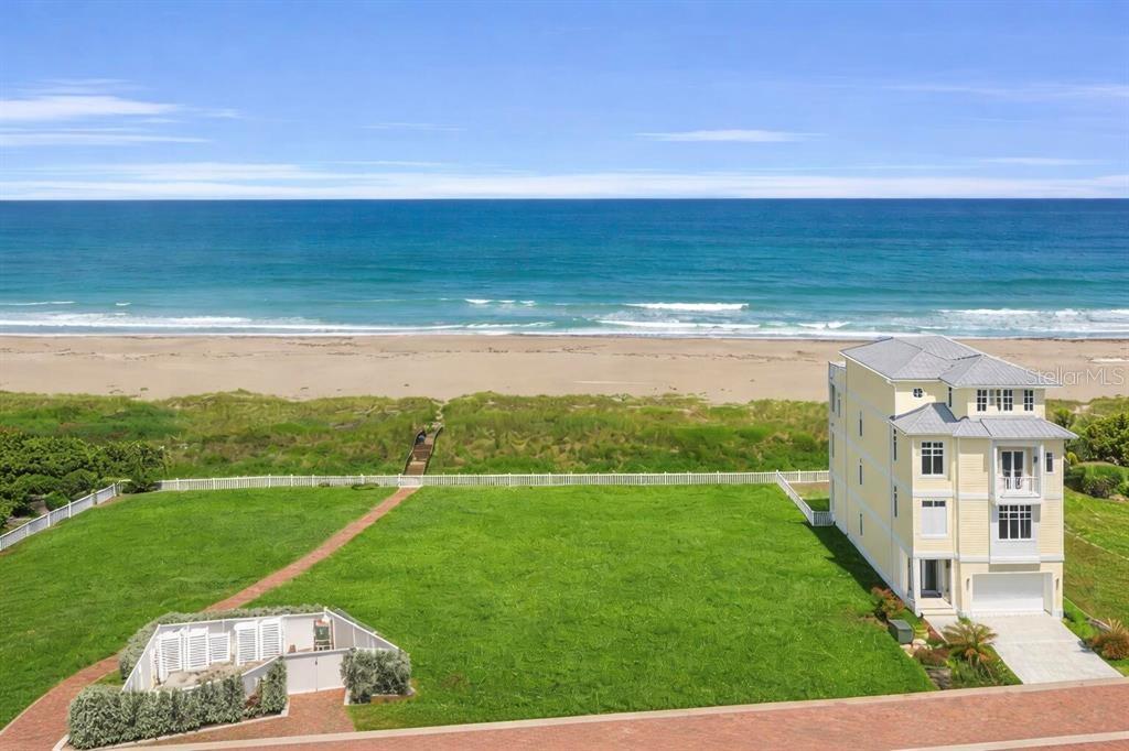 An aerial view shows a yellow three-story house on a large lawn by the beach — 5104 WATERSONG WAY, FORT PIERCE, FL