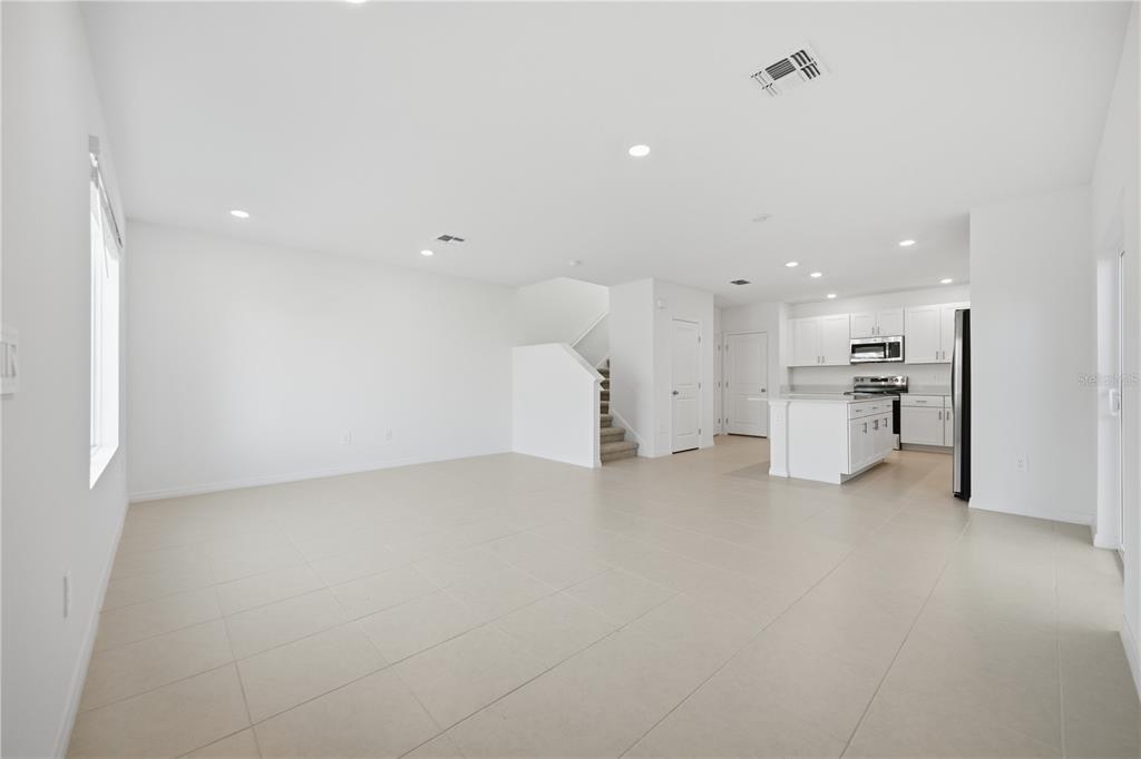 An open-concept living area features white walls, tile flooring, and an adjacent modern kitchen — 10636 SAGE CANYON DRIVE, RIVERVIEW, FL