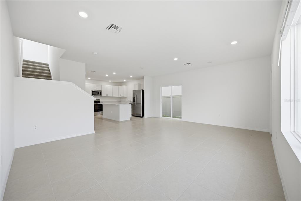 An open-concept living area features light tile flooring, white walls, and a kitchen with stainless appliances — 10636 SAGE CANYON DRIVE, RIVERVIEW, FL