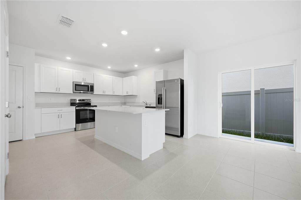 A modern kitchen features white cabinets, stainless steel appliances, a center island, and tile flooring — 10636 SAGE CANYON DRIVE, RIVERVIEW, FL