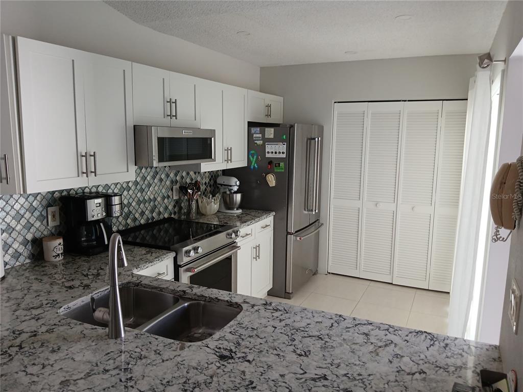 A kitchen features white cabinets, granite countertops, stainless steel appliances, and a tiled backsplash — 913 WATERSIDE LANE UNIT 913, BRADENTON, FL