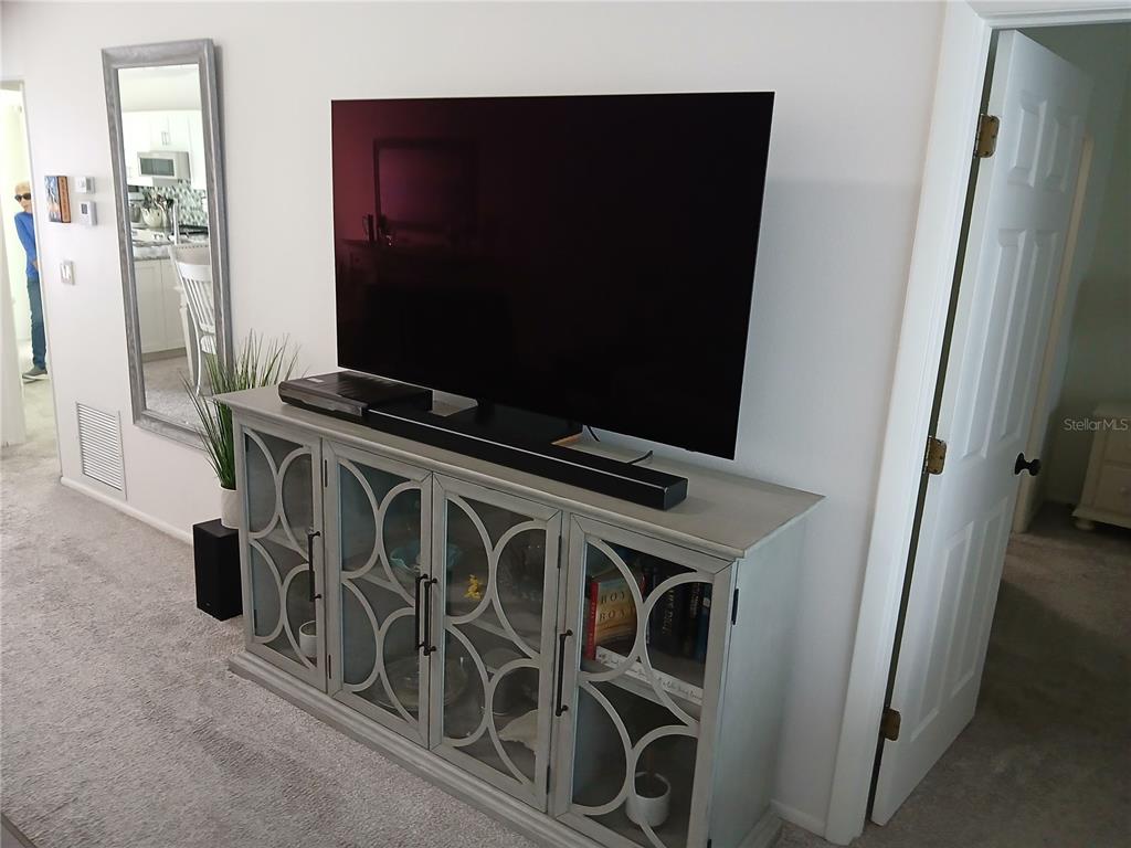 A television sits on a light-colored cabinet with glass-paneled doors in a carpeted room — 913 WATERSIDE LANE UNIT 913, BRADENTON, FL