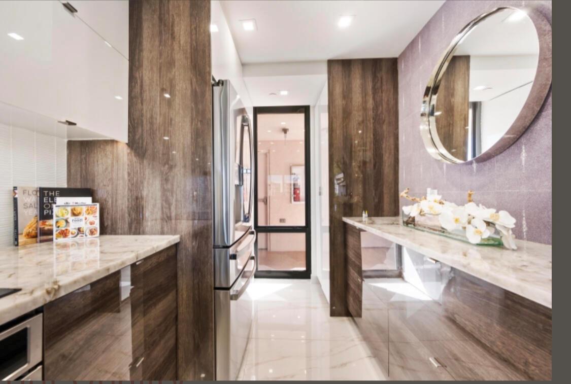 A modern kitchen featuring wood-grain cabinetry, marble countertops, stainless steel appliances, and a round mirror — 2687 N Ocean Boulevard # G506, Boca Raton FL 33431, BOCA RATON, FL