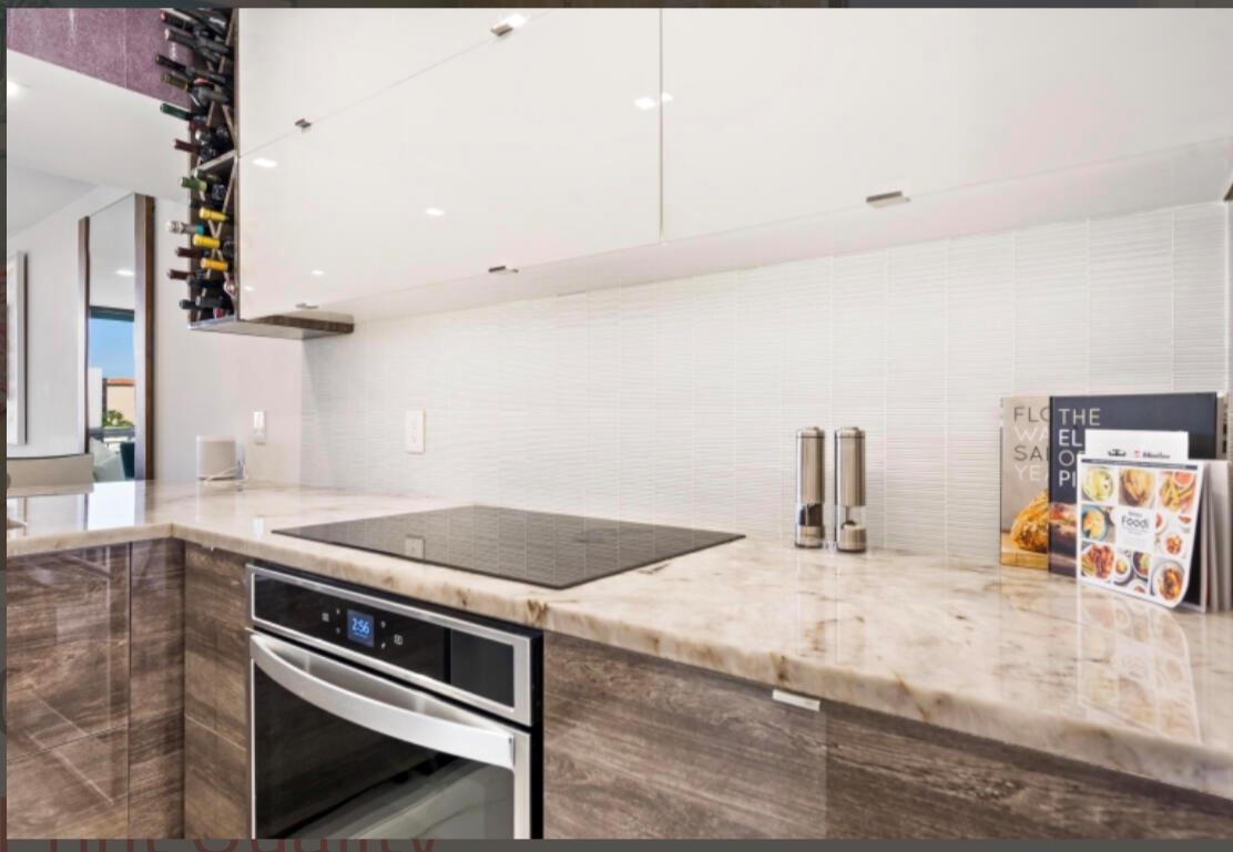 A modern kitchen features wood-grain cabinets, a marble countertop, an induction cooktop, and white backsplash — 2687 N Ocean Boulevard # G506, Boca Raton FL 33431, BOCA RATON, FL