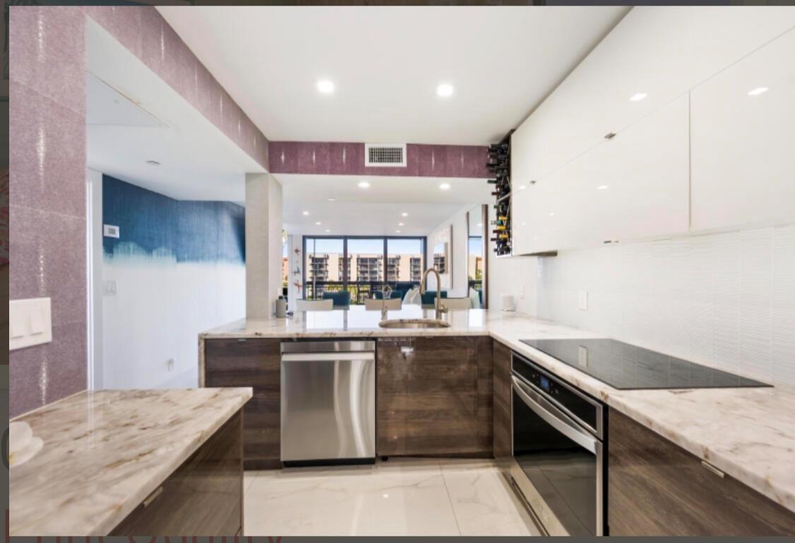 A modern kitchen features wood-grain lower cabinets, white upper cabinets, and marble countertops — 2687 N Ocean Boulevard # G506, Boca Raton FL 33431, BOCA RATON, FL
