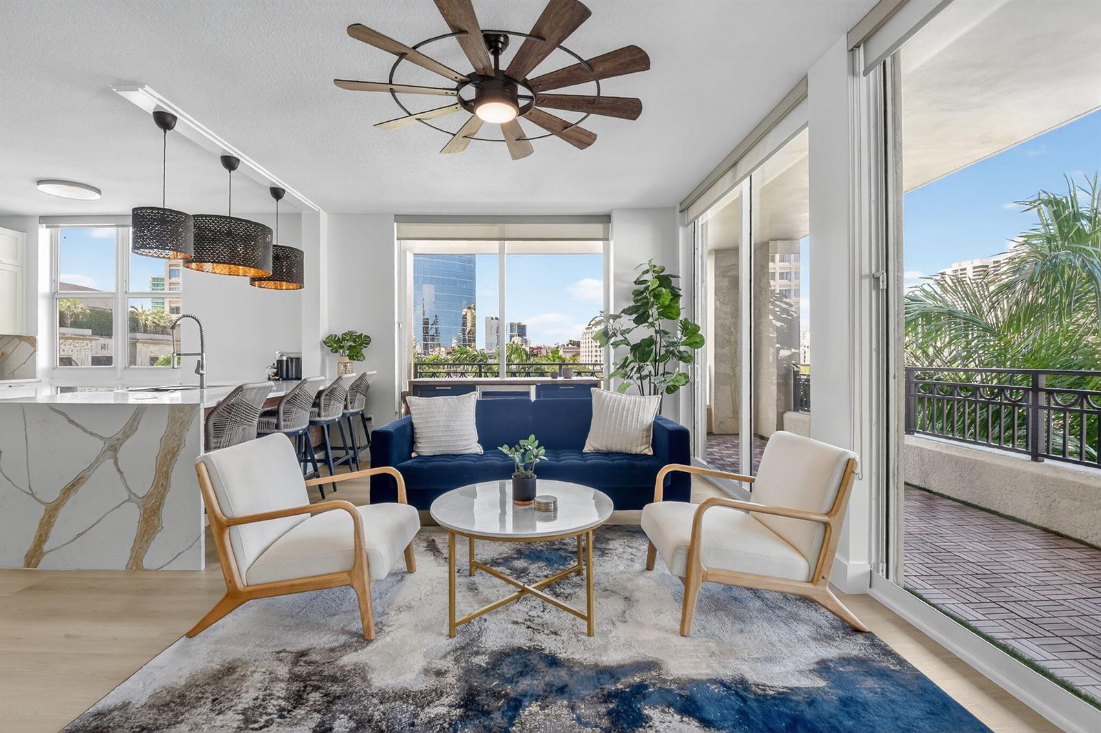 A modern living room with a blue sofa, two white chairs, and a balcony view — 550 Okeechobee Boulevard # 502, West Palm Beach FL 33401, WEST PALM BEACH, FL