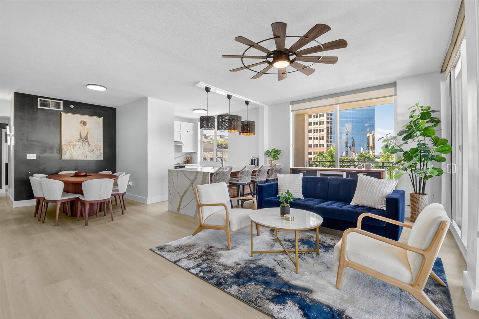 An open-concept living and dining area features a blue sofa, marble-topped island, and city views — 550 Okeechobee Boulevard # 502, West Palm Beach FL 33401, WEST PALM BEACH, FL