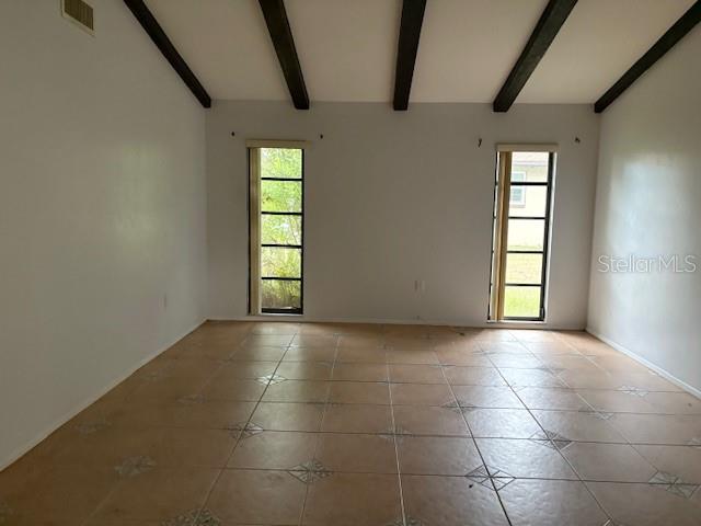 An empty room features tiled flooring, white walls, and a vaulted ceiling with exposed beams — 4051 BENT TREE BOULEVARD, SARASOTA, FL
