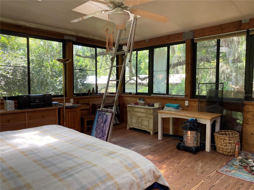 A sunroom features wood walls, a ceiling fan, a ladder, and large windows overlooking trees — 2424 NE 170TH STREET, CITRA, FL