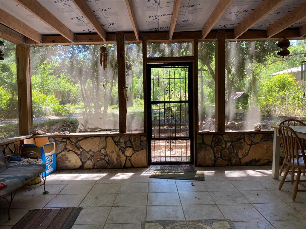 A screened-in porch features stone walls, tile flooring, and a view of the wooded yard — 2424 NE 170TH STREET, CITRA, FL