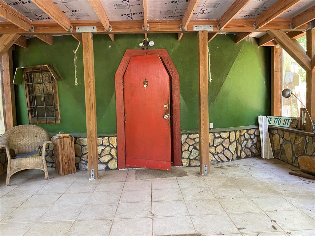 A covered porch features a red coffin-shaped door, stone wainscoting, and a green wall — 2424 NE 170TH STREET, CITRA, FL