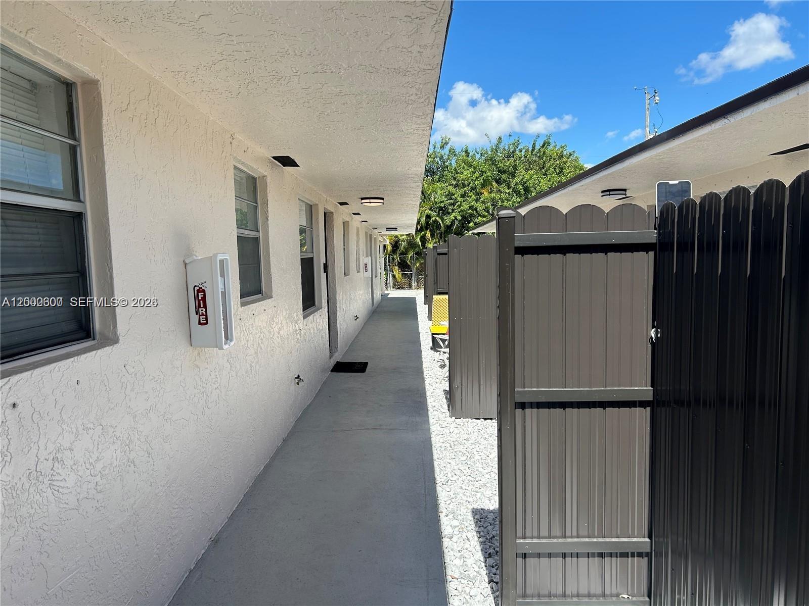 A concrete walkway runs between a white stucco building and a dark metal privacy fence — 904 SW 10th St, Hallandale Beach FL 33009, HALLANDALE BEACH, FL