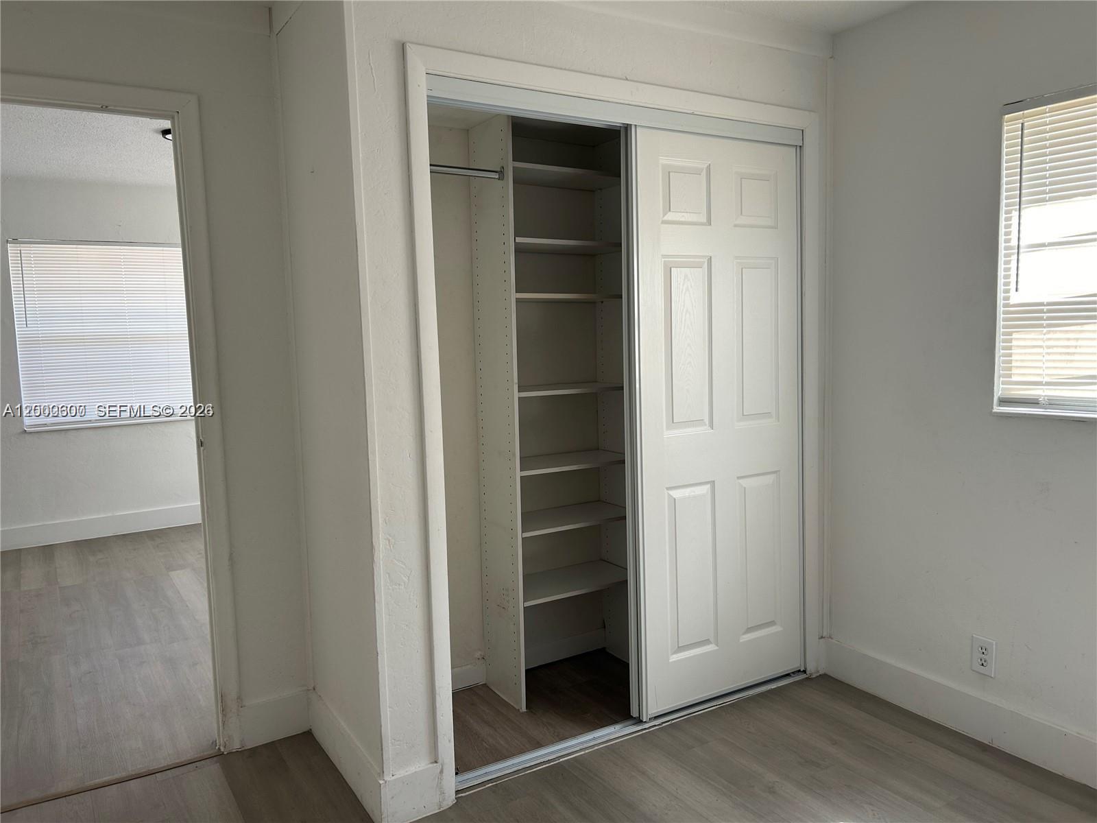 A bedroom features light wood-look flooring, white walls, and a closet with built-in shelving — 904 SW 10th St, Hallandale Beach FL 33009, HALLANDALE BEACH, FL