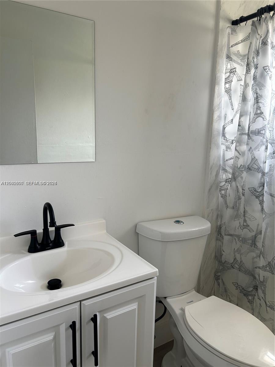 A bathroom features a white vanity with a black faucet, a toilet, and a shower curtain — 904 SW 10th St, Hallandale Beach FL 33009, HALLANDALE BEACH, FL