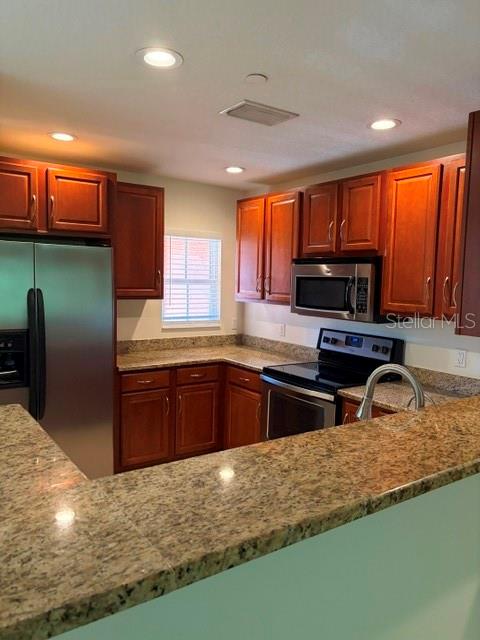 A kitchen features wood cabinets, granite countertops, stainless steel appliances, and recessed lighting — 8858 WHITE SAGE LOOP, LAKEWOOD RANCH, FL
