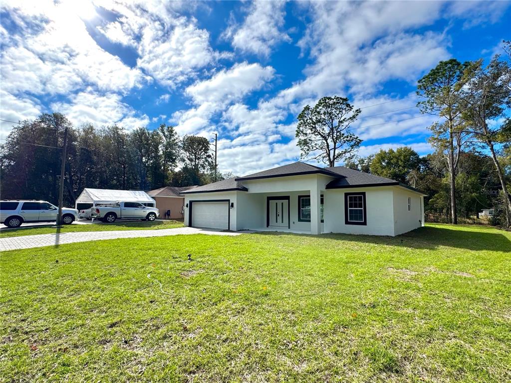 A white single-story house with a black roof and a paved driveway under a cloudy sky — 9082 N CORTLANDT DRIVE, CITRUS SPRINGS, FL