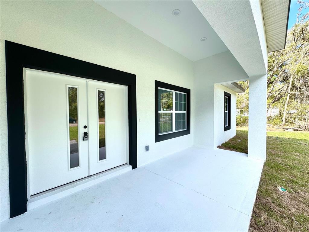 A white covered porch features a double front door and a window with black trim — 9082 N CORTLANDT DRIVE, CITRUS SPRINGS, FL