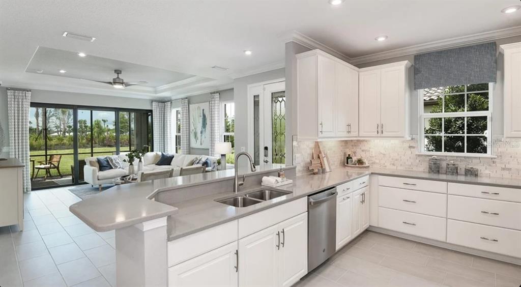 A bright living room features a white sectional sofa, a round coffee table, and large sliding glass doors — 13308 SANTINI CIRCLE, ENGLEWOOD, FL