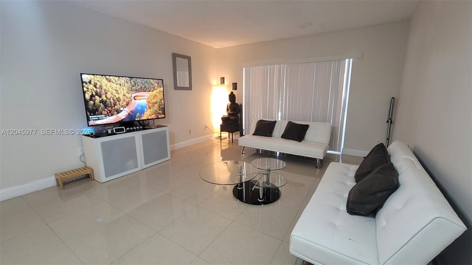 A living room features white tile floors, two white sofas, and a television on a stand — 7705 Camino Real # 215, Miami FL 33143, MIAMI, FL