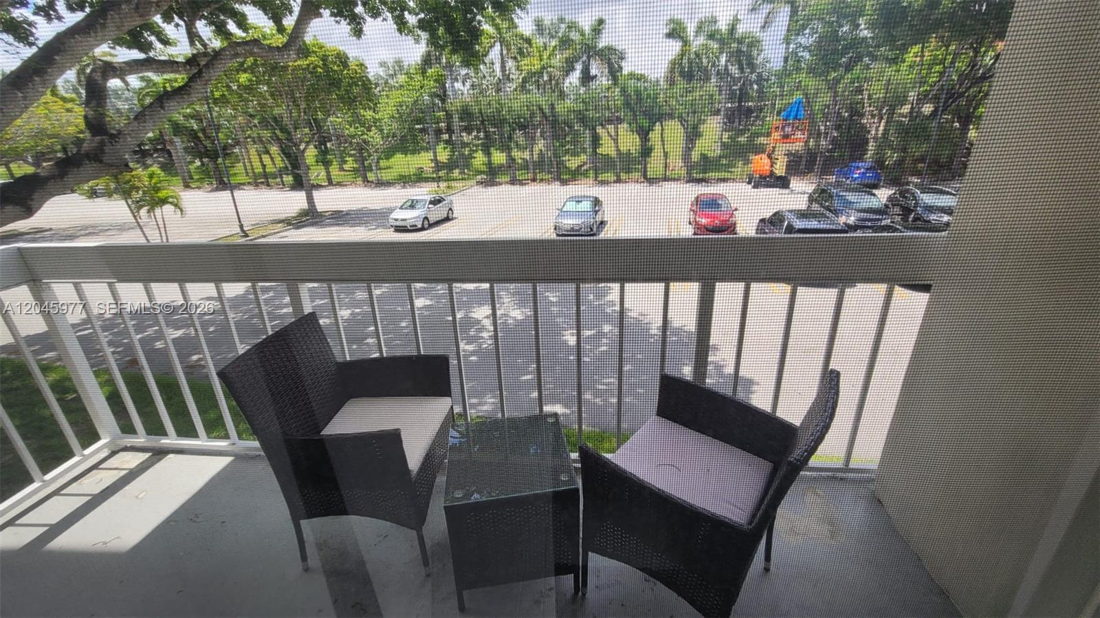 A balcony features two wicker chairs and a small table overlooking a parking lot — 7705 Camino Real # 215, Miami FL 33143, MIAMI, FL