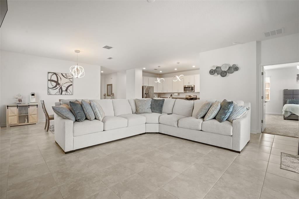 A spacious living room features a large white sectional sofa, tile flooring, and an open kitchen — 5256 DAGENHAM DRIVE, DAVENPORT, FL