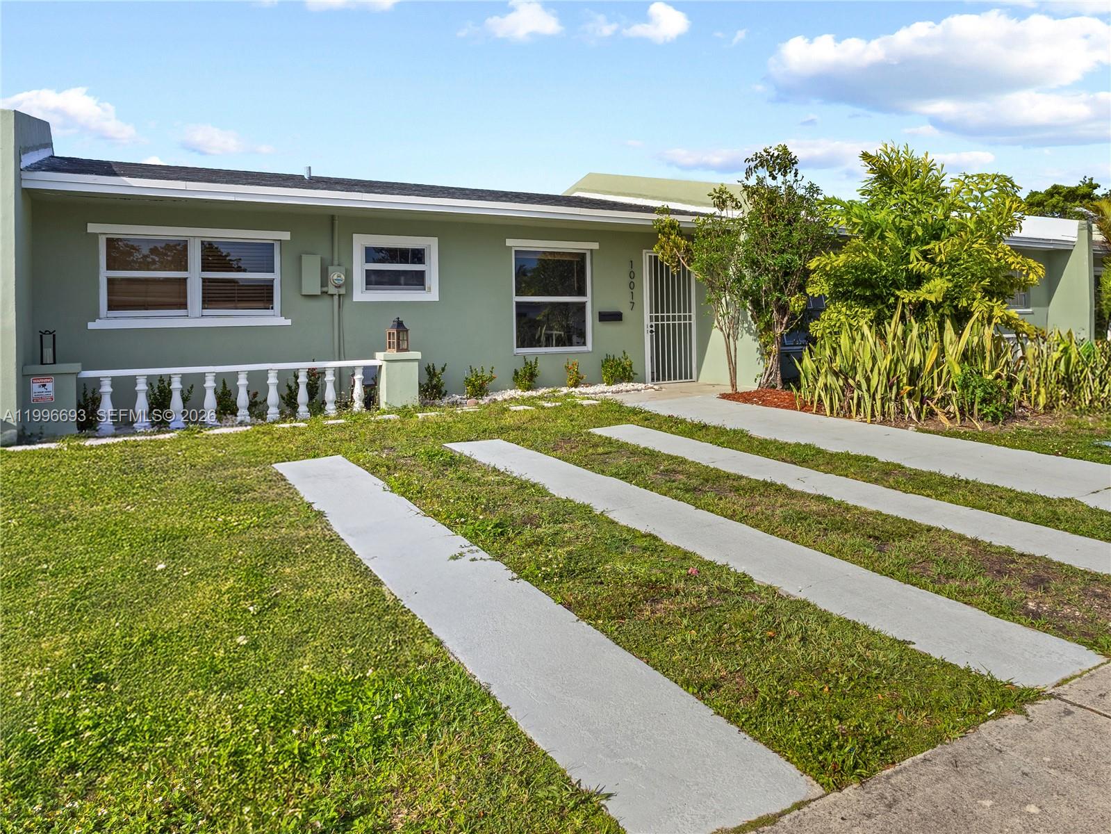 A light green single-story house features a white balustrade, concrete driveway strips, and landscaping — 10017 SW 23rd Ter, Miami FL 33165, MIAMI, FL