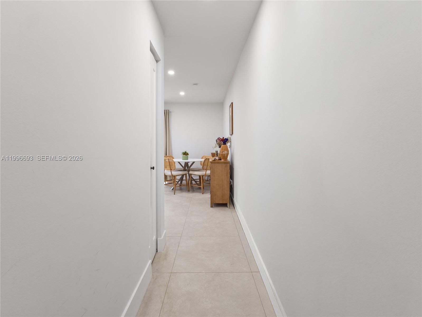 A hallway with light-colored tile flooring leads to a dining area with a round table — 10017 SW 23rd Ter, Miami FL 33165, MIAMI, FL