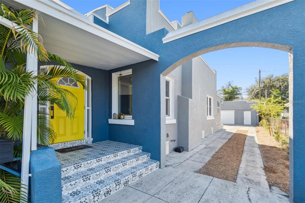 A bright yellow front door is centered above tiled steps leading to a blue house — 1120 17TH AVENUE N, ST PETERSBURG, FL