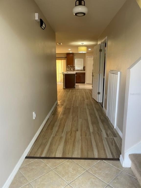 A hallway with tile flooring leads to a kitchen featuring wood cabinets and an island — 2950 WILLOWLEAF LANE, WESLEY CHAPEL, FL
