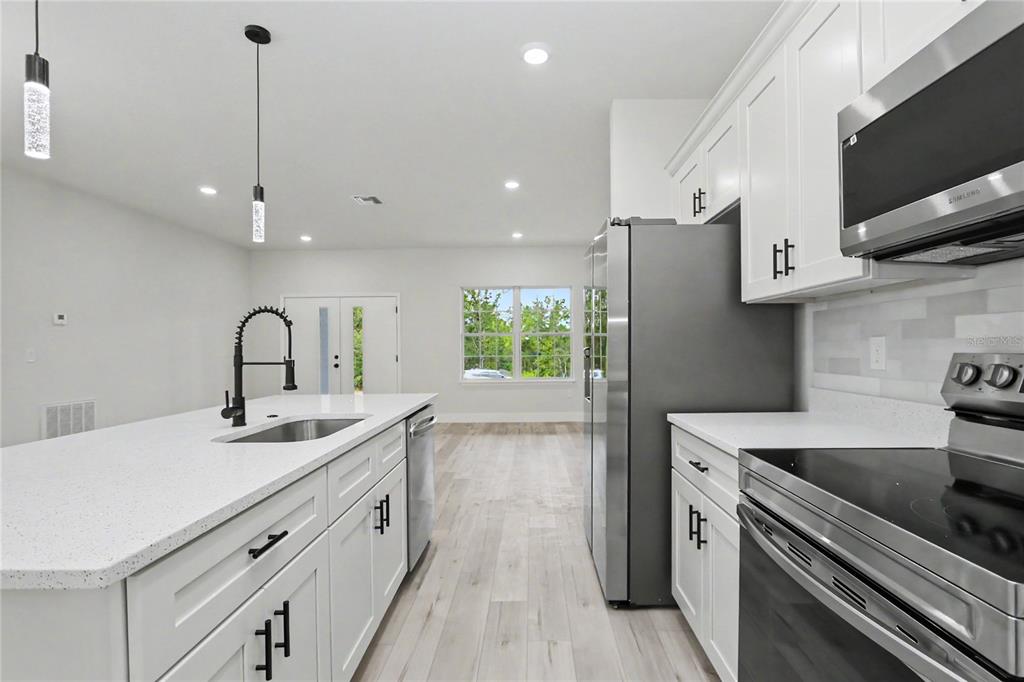 A modern kitchen features white cabinets, stainless steel appliances, a quartz island, and light flooring — 7945 N IBSEN DRIVE, CITRUS SPRINGS, FL