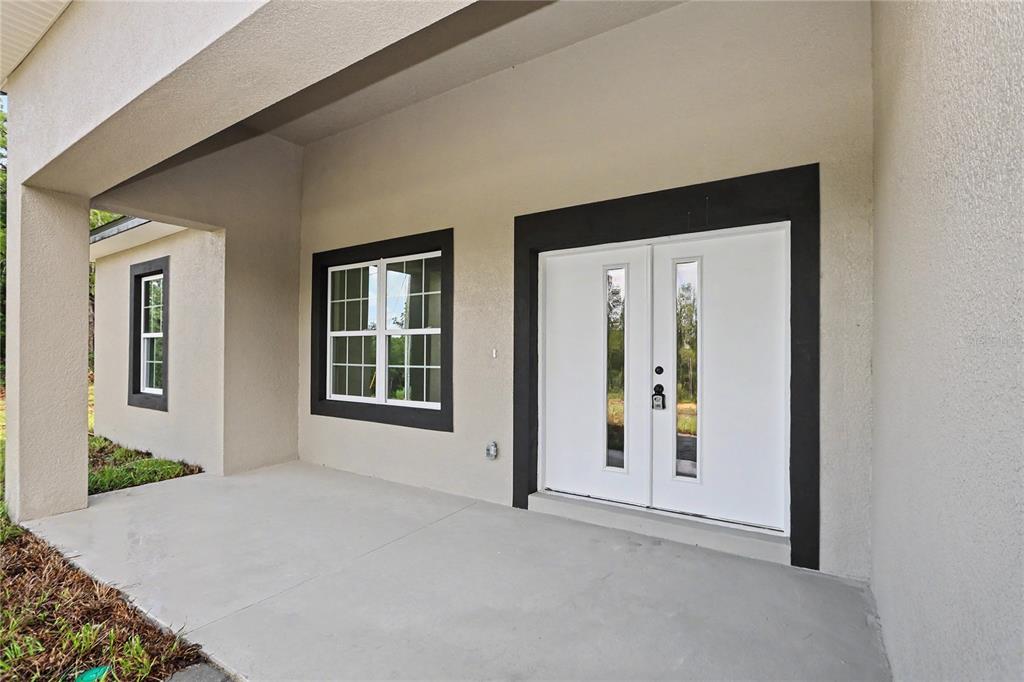 A covered concrete porch features a white double front door and two windows with black trim — 7945 N IBSEN DRIVE, CITRUS SPRINGS, FL