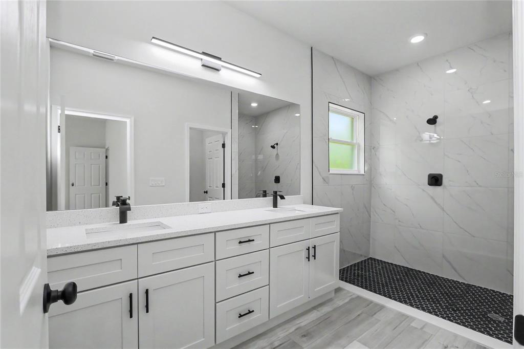 A modern bathroom features a double vanity with white cabinets, marble-look walls, and a shower — 7945 N IBSEN DRIVE, CITRUS SPRINGS, FL