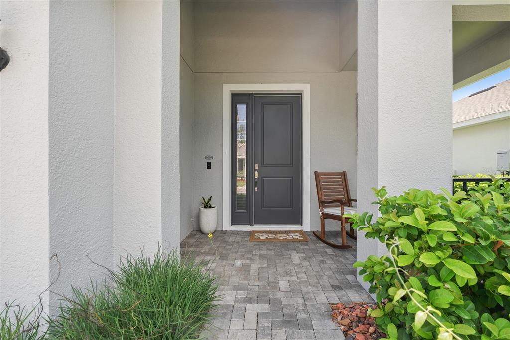 A gray front door with a side window sits on a paved porch with a rocker — 2316 SIRENA LANE, MOUNT DORA, FL