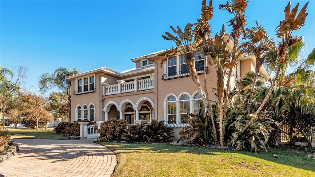 A two-story beige house with a paved driveway and arched windows under a clear sky — 1665 BLUE HERON LANE, LAKELAND, FL
