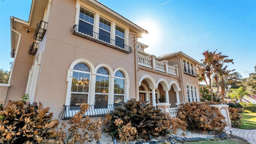 A two-story tan stucco house features arched windows, a balcony, and decorative iron railings — 1665 BLUE HERON LANE, LAKELAND, FL