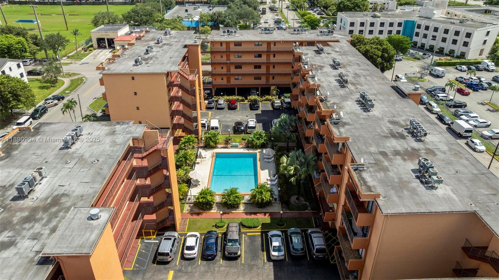 An aerial view shows a multi-story apartment complex with a central swimming pool and parking — 1800 W 54th St # 109, Hialeah FL 33012, HIALEAH, FL