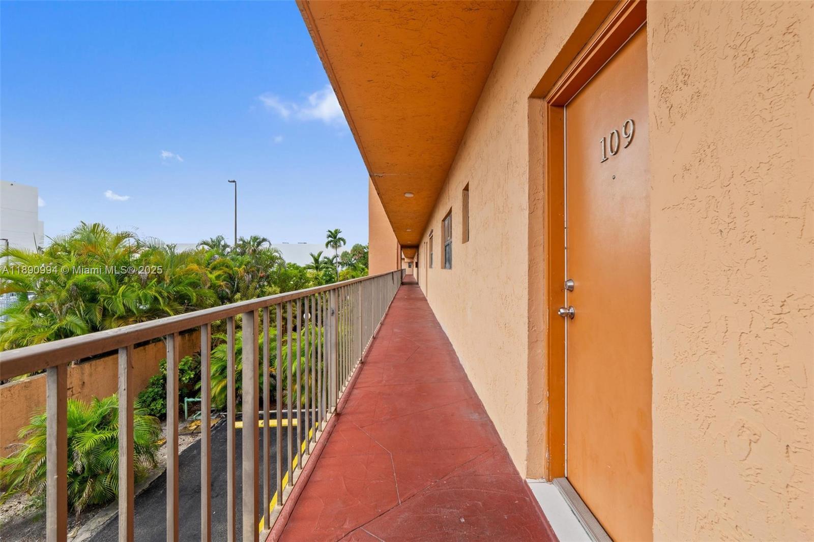 An exterior walkway with a metal railing leads past an orange door marked 109 — 1800 W 54th St # 109, Hialeah FL 33012, HIALEAH, FL