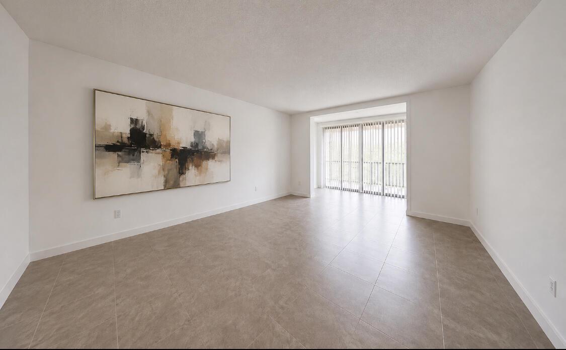An empty living room features large beige floor tiles, white walls, and a large abstract painting — 3740 Inverrary Drive # 3g, Lauderhill FL 33319, LAUDERHILL, FL
